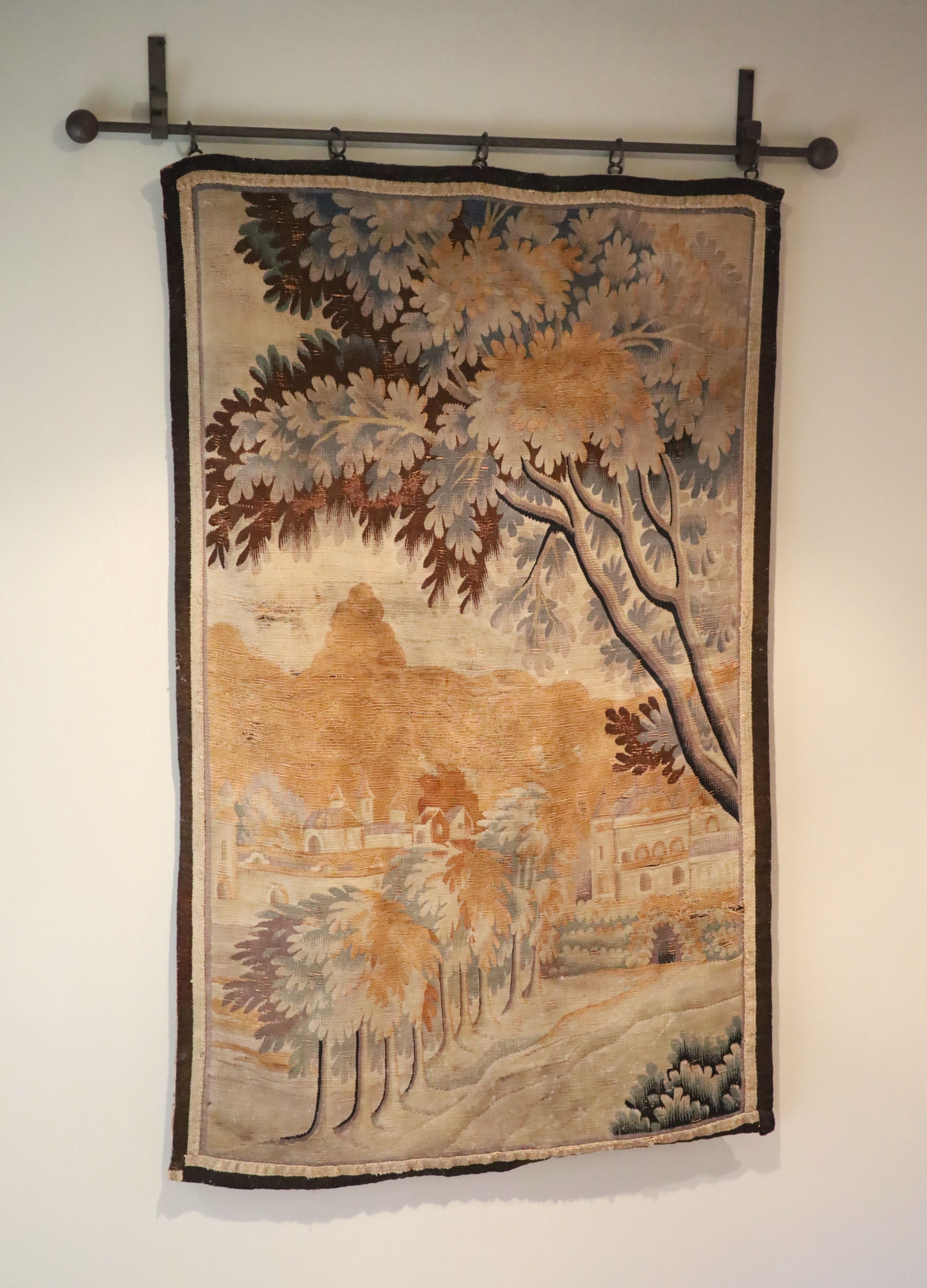 A French tapestry wall hanging, decorated with a town and trees, 125 x 79cm, with associated wrought iron hanging rail